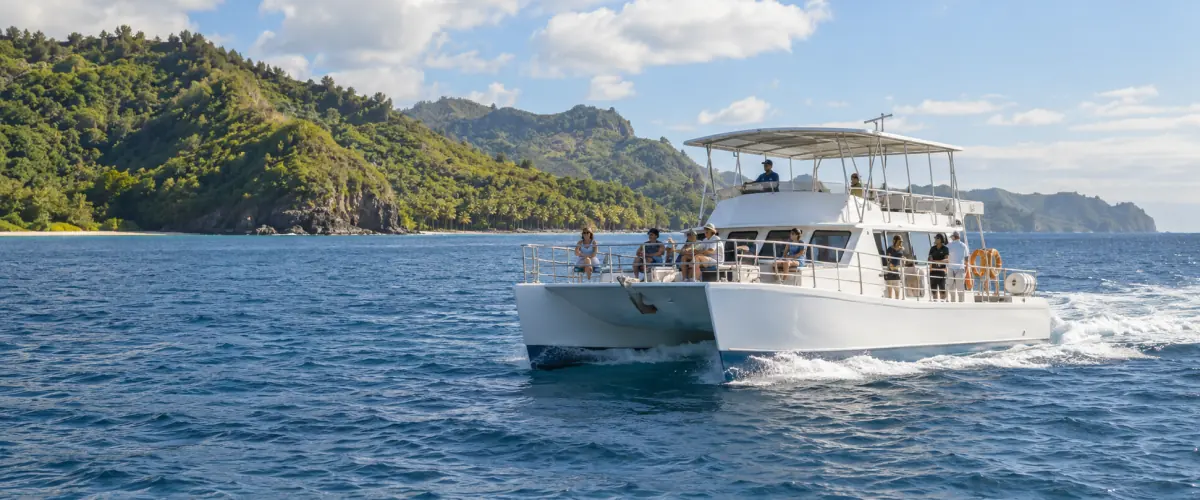 Passengers aboard a white tour boat traveling near a green island coastline.