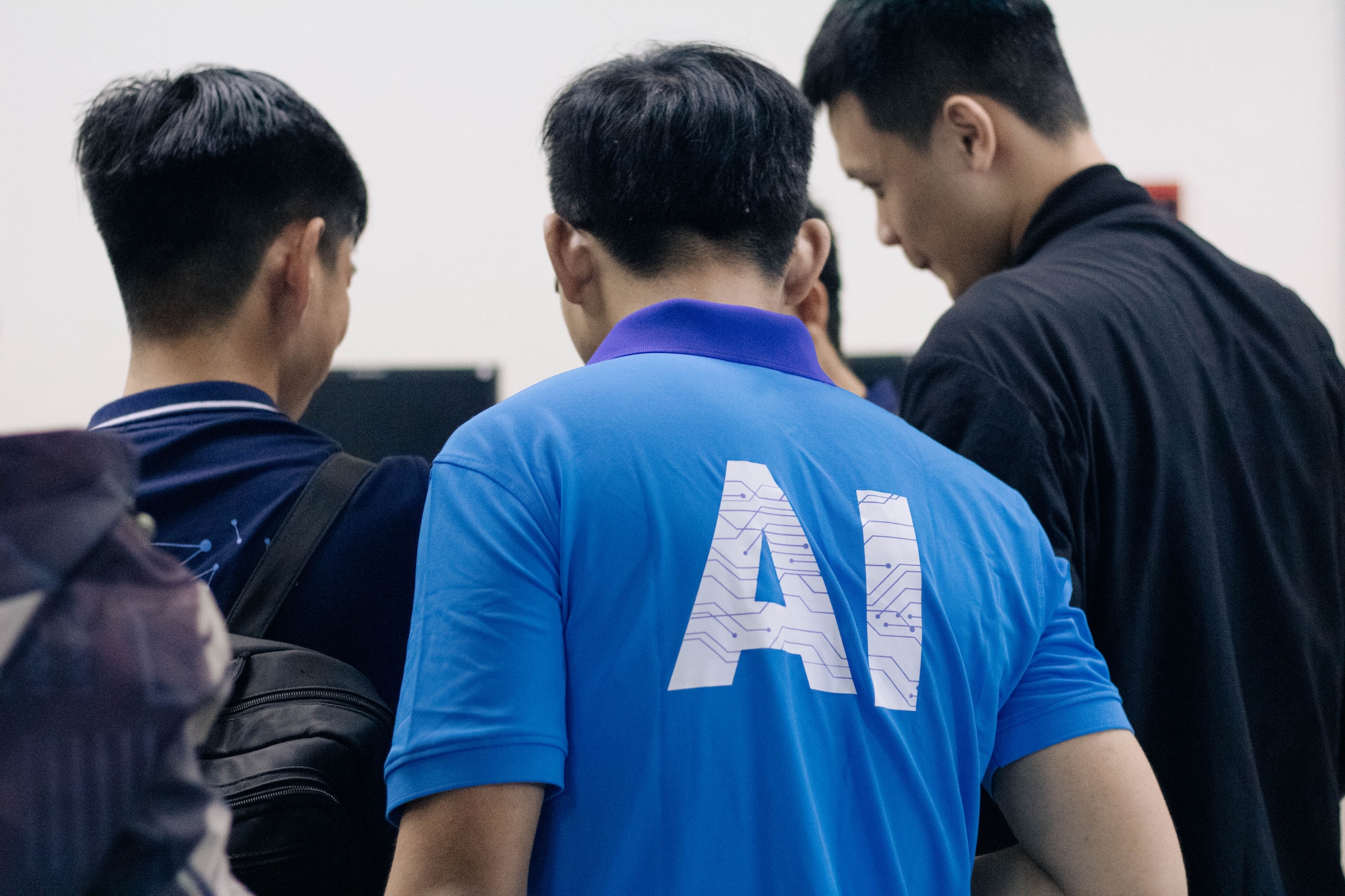 Navigating AI, People looking at something with a guy wearing an AI shirt