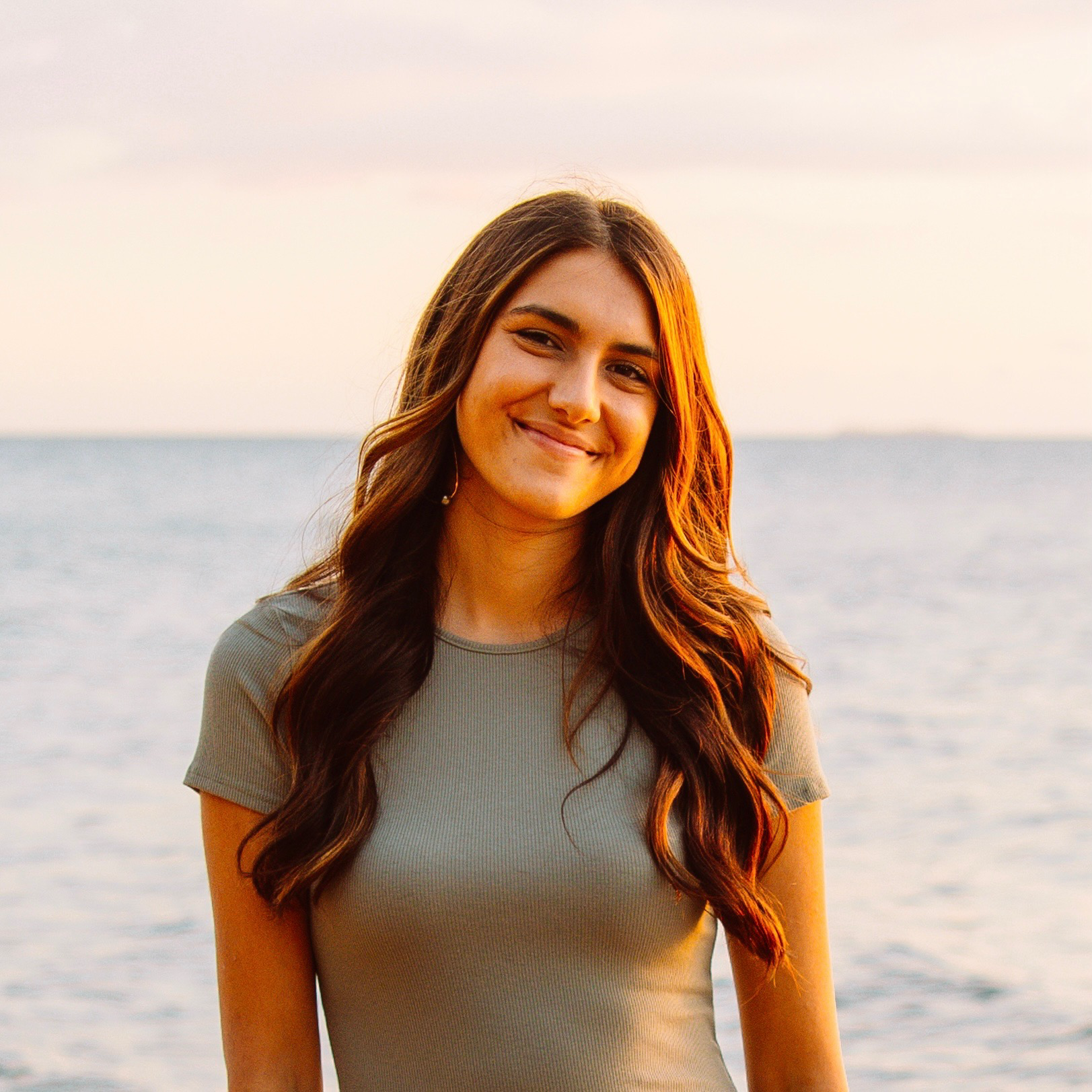 Digital Reach Smiling young woman with long brown hair at the beach during sunset.