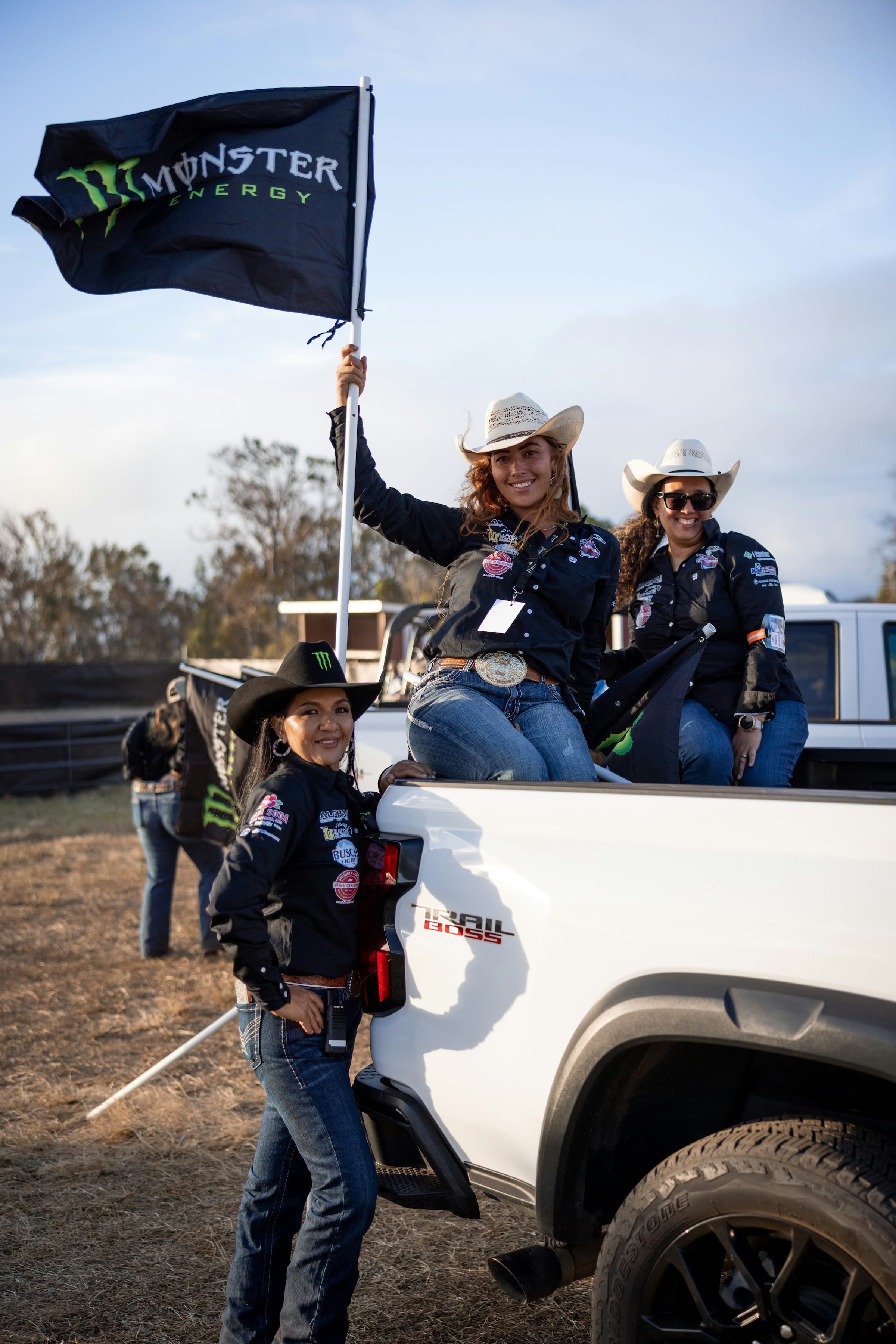 Digital Reach VLKL5pVzz3k Unsplash • Digital Reach Digital Reach, Cowgirl team in a truck bed holding a Monster Energy flag, rodeo event.